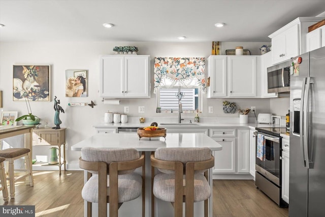 kitchen featuring a kitchen bar, stainless steel appliances, white cabinetry, and sink