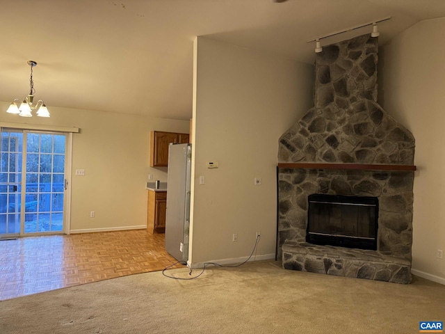 unfurnished living room with rail lighting, vaulted ceiling, light parquet floors, a chandelier, and a stone fireplace