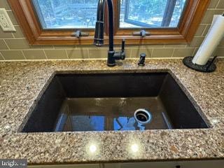 room details featuring decorative backsplash, sink, and light stone counters