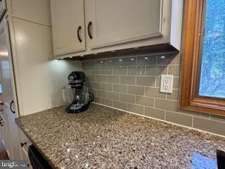 room details with tasteful backsplash, white cabinetry, and light stone counters