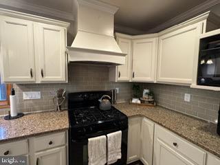 kitchen with gas stove, backsplash, white cabinetry, and premium range hood