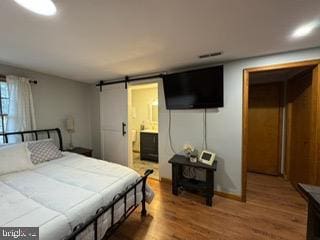 bedroom featuring hardwood / wood-style floors, a barn door, and ensuite bathroom