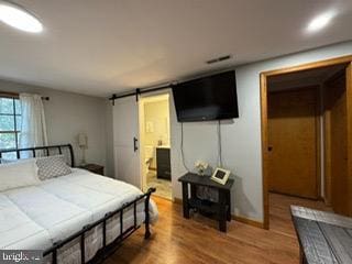 bedroom featuring connected bathroom, a barn door, and hardwood / wood-style floors