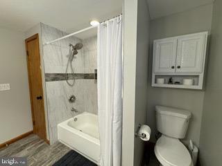 bathroom featuring toilet, hardwood / wood-style floors, and shower / tub combo with curtain