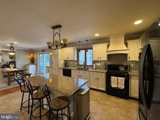 kitchen featuring stove, black fridge, custom range hood, pendant lighting, and a chandelier