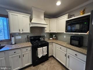 kitchen with light stone countertops, white cabinets, black appliances, and custom exhaust hood