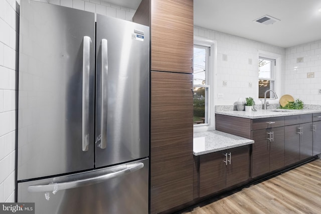 kitchen with sink, stainless steel refrigerator, dark brown cabinetry, light stone counters, and light hardwood / wood-style floors