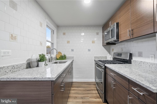 kitchen featuring hardwood / wood-style floors, sink, decorative backsplash, light stone counters, and stainless steel appliances