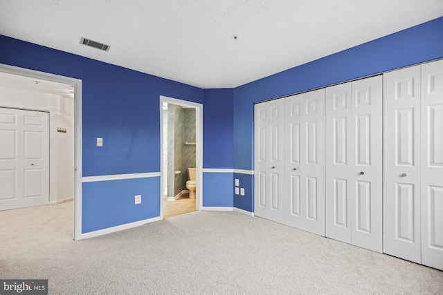 unfurnished bedroom featuring light colored carpet, ensuite bathroom, a closet, and a textured ceiling