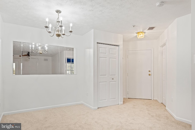 empty room with an inviting chandelier, light carpet, and a textured ceiling