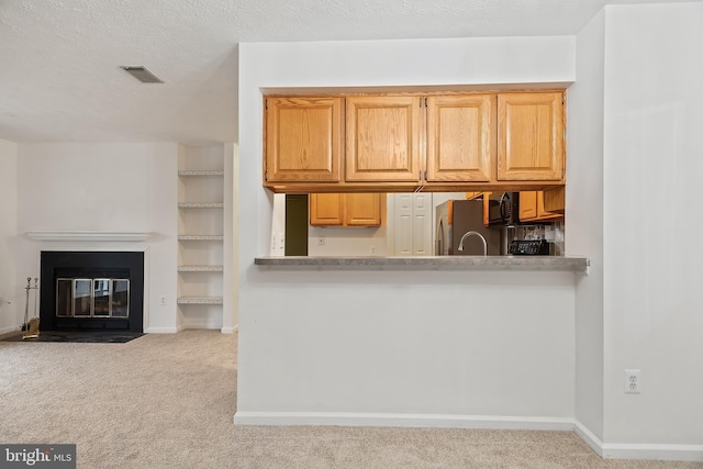 kitchen with light carpet, stainless steel fridge, a textured ceiling, and light brown cabinets