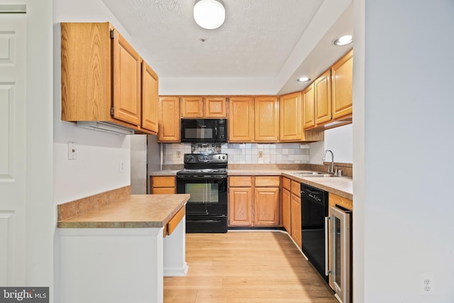 kitchen featuring wine cooler, sink, black appliances, light hardwood / wood-style flooring, and backsplash