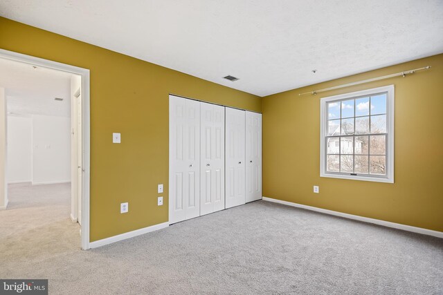 unfurnished bedroom with light carpet, a closet, and a textured ceiling