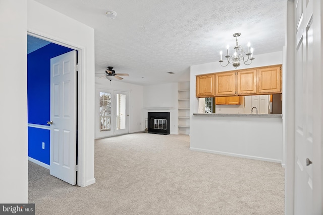 unfurnished living room featuring light colored carpet, ceiling fan with notable chandelier, and a textured ceiling