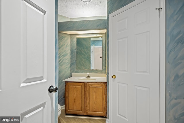 bathroom with hardwood / wood-style flooring, vanity, toilet, and a textured ceiling