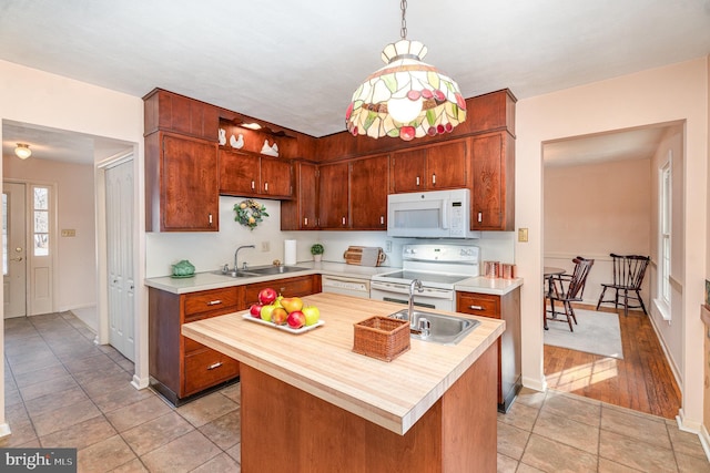 kitchen with a center island with sink, decorative light fixtures, white appliances, and sink