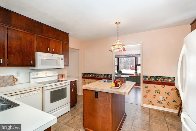 kitchen with white appliances, sink, pendant lighting, light tile patterned floors, and an island with sink