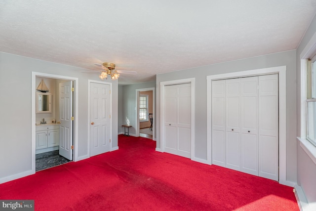 unfurnished bedroom with carpet, ensuite bathroom, a textured ceiling, two closets, and ceiling fan