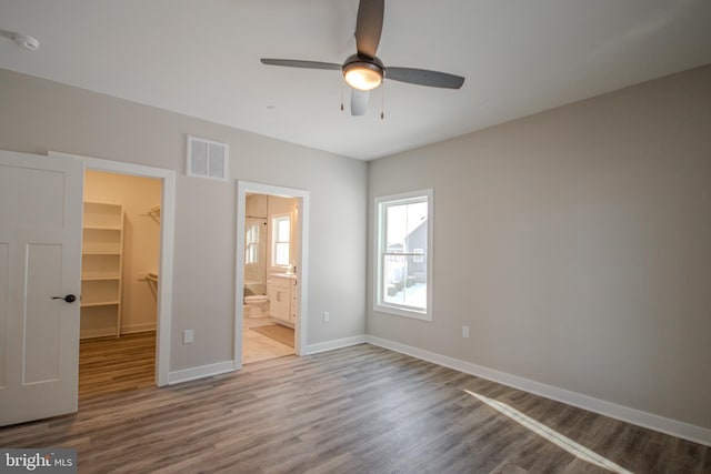 unfurnished bedroom with hardwood / wood-style floors, ceiling fan, a spacious closet, connected bathroom, and a closet