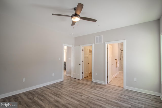 unfurnished bedroom featuring connected bathroom, light hardwood / wood-style flooring, a spacious closet, and ceiling fan