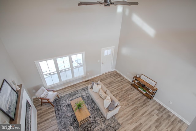 living room featuring ceiling fan, light hardwood / wood-style floors, and a high ceiling