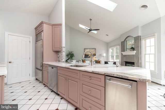 kitchen featuring kitchen peninsula, ceiling fan, appliances with stainless steel finishes, lofted ceiling with skylight, and sink