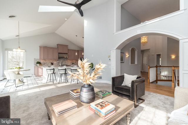 living room with light carpet, ceiling fan, sink, and high vaulted ceiling