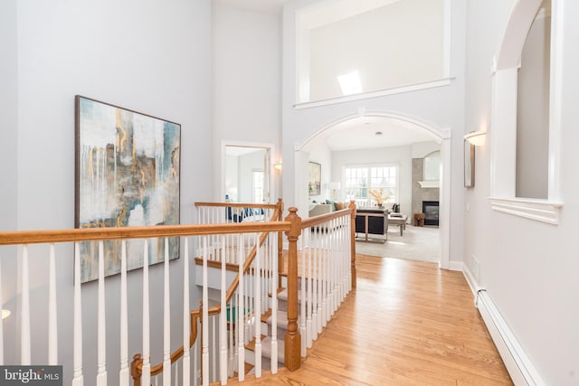 hallway featuring a high ceiling, a baseboard heating unit, and light wood-type flooring