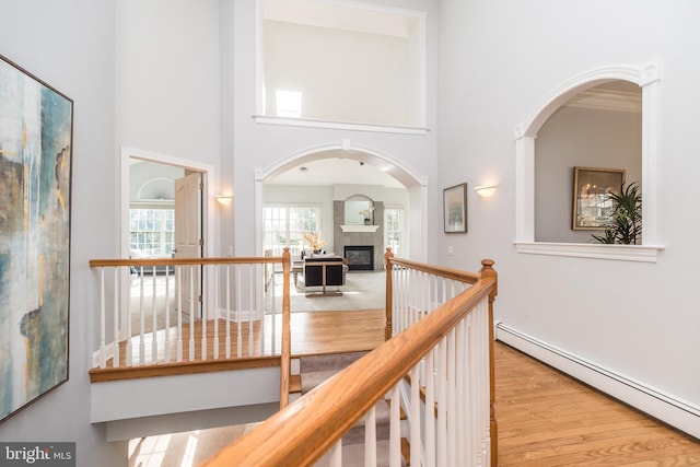 hall featuring light wood-type flooring, a baseboard heating unit, a high ceiling, and ornamental molding