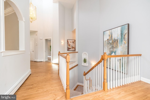 hallway featuring an inviting chandelier, a baseboard heating unit, a towering ceiling, crown molding, and light hardwood / wood-style flooring