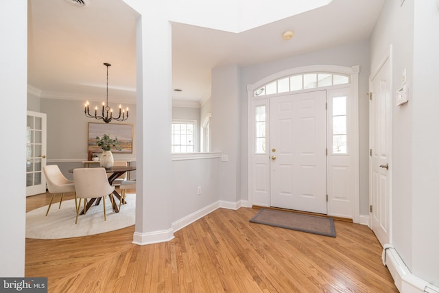 foyer entrance with a baseboard heating unit, ornamental molding, light hardwood / wood-style flooring, and a notable chandelier