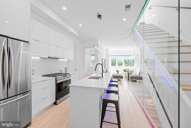 kitchen with sink, light hardwood / wood-style floors, a center island with sink, white cabinets, and appliances with stainless steel finishes