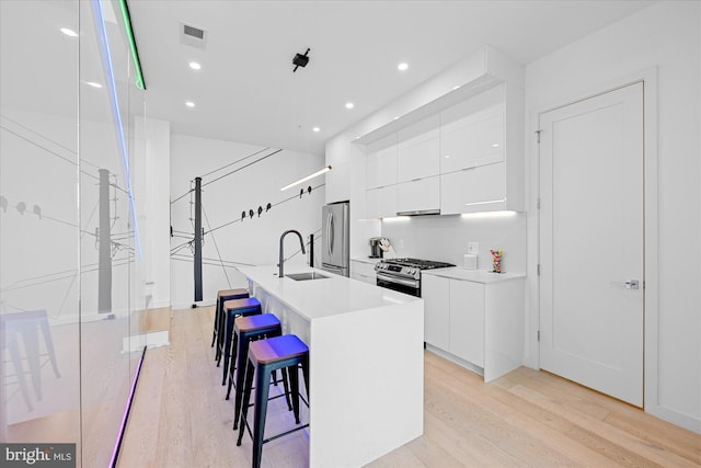 kitchen featuring white cabinetry, sink, stainless steel appliances, a kitchen bar, and a kitchen island with sink