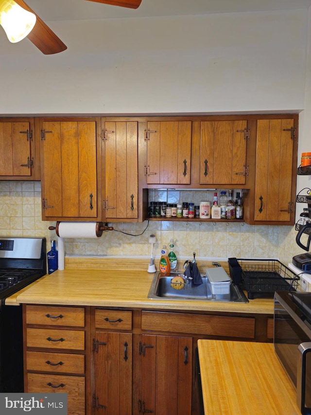 kitchen featuring gas range, backsplash, ceiling fan, and sink