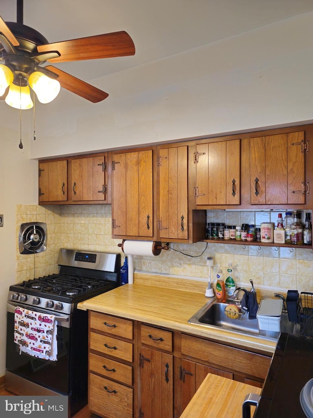 kitchen with stainless steel gas stove, ceiling fan, decorative backsplash, and sink