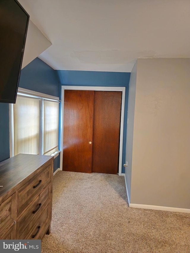 unfurnished bedroom featuring carpet, a closet, and lofted ceiling