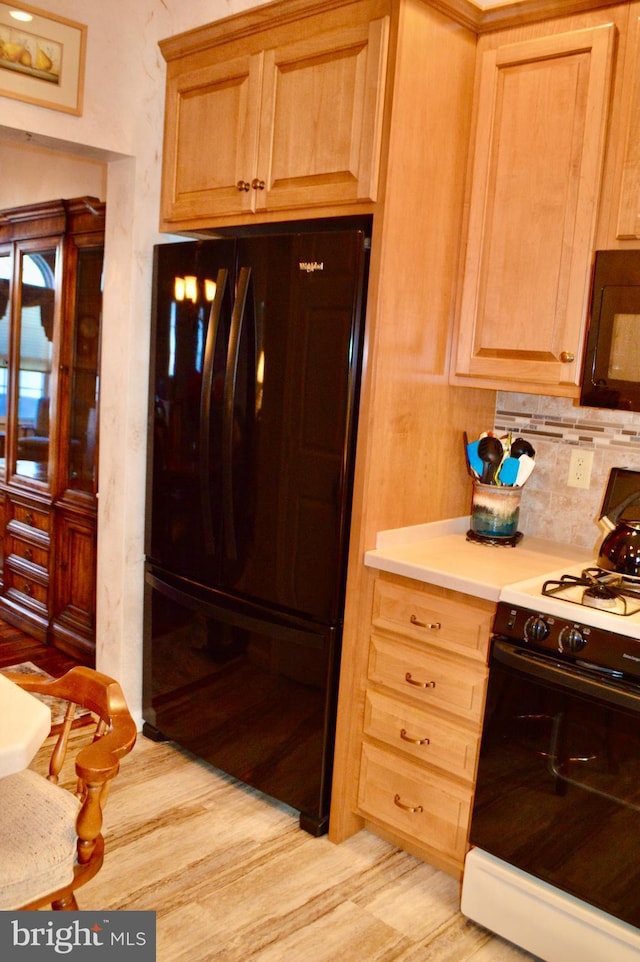 kitchen with light brown cabinets, black fridge, backsplash, light hardwood / wood-style floors, and white gas range oven