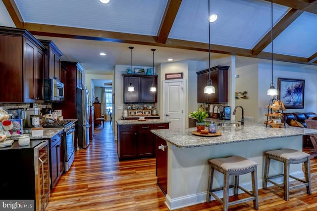 kitchen with hanging light fixtures, light hardwood / wood-style floors, kitchen peninsula, and appliances with stainless steel finishes