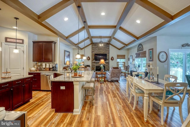 kitchen with a kitchen bar, light stone counters, hanging light fixtures, stainless steel dishwasher, and a kitchen island