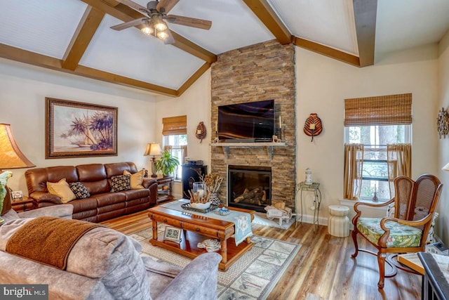 living room featuring a stone fireplace, plenty of natural light, lofted ceiling with beams, and light wood-type flooring