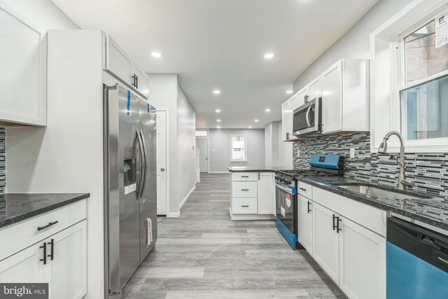 kitchen with stainless steel appliances, dark stone countertops, white cabinetry, and sink