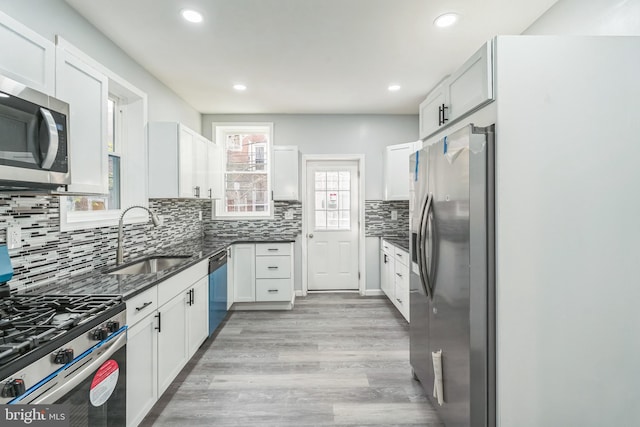 kitchen with white cabinets, stainless steel appliances, dark stone counters, sink, and light wood-type flooring