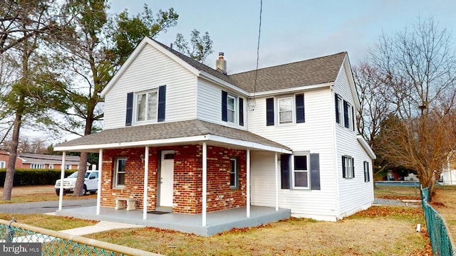 view of front of house with a shingled roof, a chimney, a porch, and brick siding