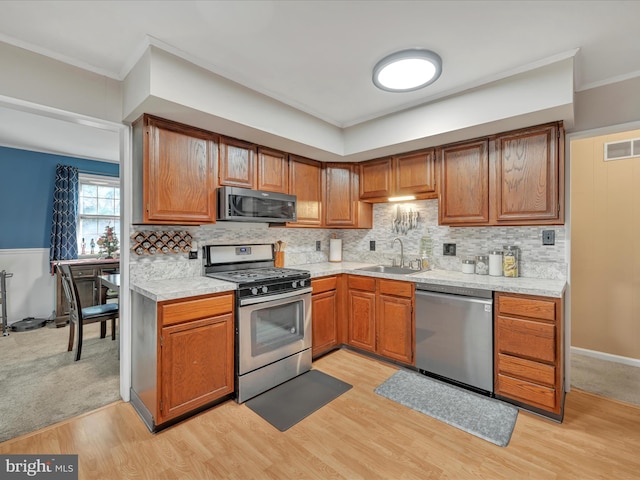 kitchen with crown molding, sink, light wood-type flooring, tasteful backsplash, and stainless steel appliances