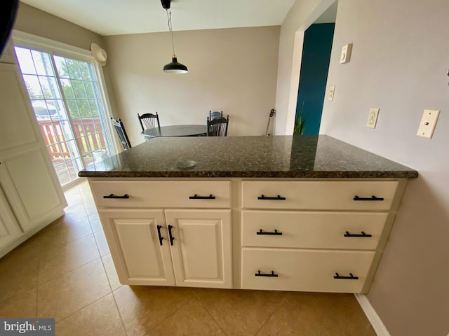 kitchen with pendant lighting, light tile patterned floors, white cabinetry, and dark stone counters