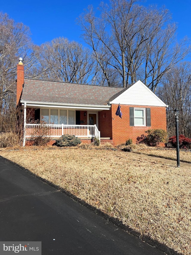 ranch-style home featuring brick siding, covered porch, and a chimney