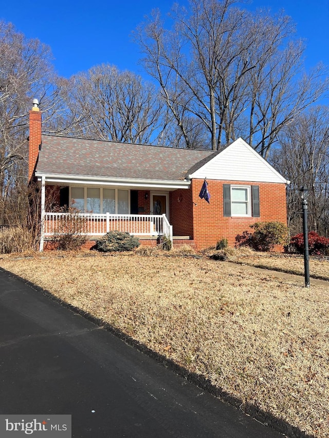 single story home featuring covered porch, a chimney, and brick siding