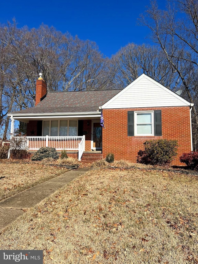 single story home with a chimney, a front lawn, a porch, and brick siding