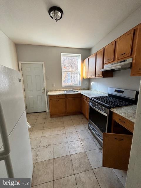 kitchen featuring stainless steel range with gas cooktop, sink, light tile patterned floors, and white refrigerator