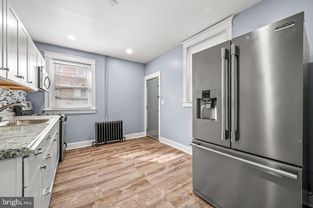 kitchen with stainless steel appliances, light wood-type flooring, radiator heating unit, white cabinets, and sink